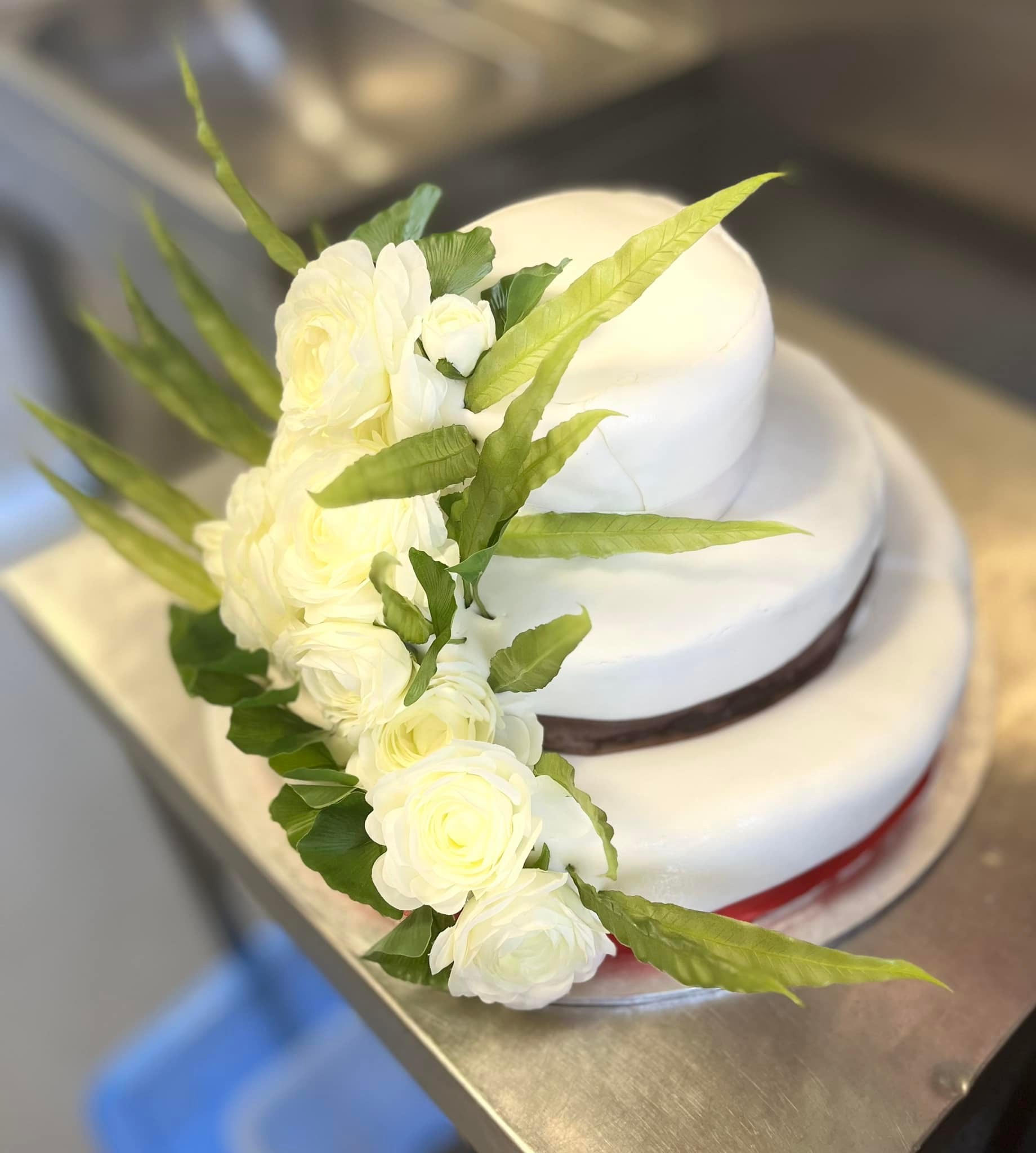 Close-up of a gluten-free wedding cake by The Empowered Oven, finished with fresh white roses and greenery
